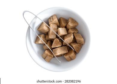 View From Above Of Brown Sugar Cubes In A Bowl With A Pair Of Tongs For Serving, Isolated On White