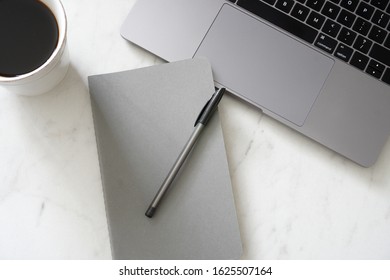 VIew From Above Of A Closed Gray Notebook With A Pen, Laptop And A Mug Of Coffee; Modern; Minimal; Office Setting