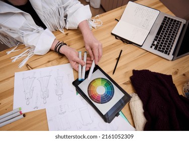 View from above to a fashion designer workplace: digital tablet with color wheel, colored markers, fashion sketches, laptop on wooden table in fashion design workshop or tailoring atelier - Powered by Shutterstock