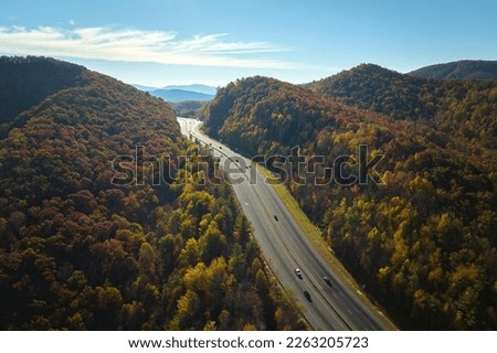 View from above of I-40 freeway route in North Carolina leading to Asheville thru Appalachian mountains with yellow fall woods and fast moving trucks and cars. Interstate transportation concept