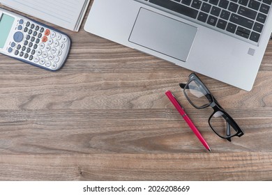 View From Above Of Laptop, Eyeglasses, Pen, Notebook And Calculator On The Wooden Background.  Negative Space Concept.  Noise Is Visible Due To The Texture Of The Subjects