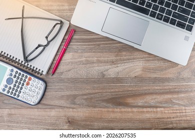 View From Above Of Laptop, Pen, Notebook, Eyeglasses And Calculator On The Wooden Background. Negative Space Concept. Noise Is Available Due To The Texture Of The Subjects