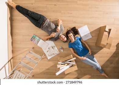 view from above, looking at the camera a young couple lying on the floor of their new home, there are blueprints to help them to think about their new interior decoration - Powered by Shutterstock