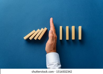 Blick von oben von männlicher Hand, die einbrechende Dominosteine in ein konzeptionelles Bild des Wirtschaftskrisenmanagements einmischt. Auf sechsblauem Hintergrund.