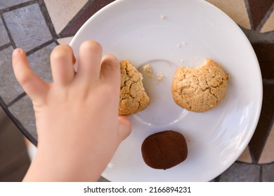 The view from above on the hand of the child taking homemade cookies from a white plate.