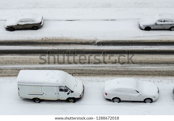 View from above on road rut\
and cars parked on roadside, covered with snow during winter\
snowfall