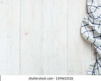 View From Above On White Wooden Table With Linen Kitchen Towel Or Textile Napkin. Blue Tablecloth On White Wood Tabletop. Copy Space For Text. Can Use As Mock Up For Design.