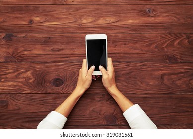 View From Above On Womans Hands Typing On Smartphone Over Wooden Brown Table