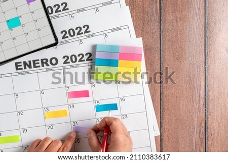 View from above of a person's hand using colored post it notes to write down the most important activities to do during the month. Calendar in Spanish. Concept plans and objectives, goal fulfillment