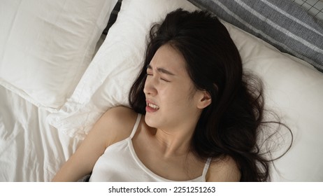 view from above restless Taiwanese female awaking from bad dream and catching her breath while staring upward with a frightened face on bed - Powered by Shutterstock