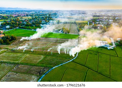 View from above of rice fields with small fire burning spots and smoke of the countryside in a blur background of town and village from afar in a evening of Chiengmai, Thailand