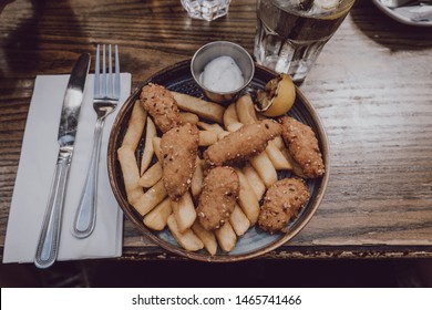 View From Above Of Scampi And Chips Popular British Pub Food, On A Plate, Cutlery Next To It, On A Wooden Table. 