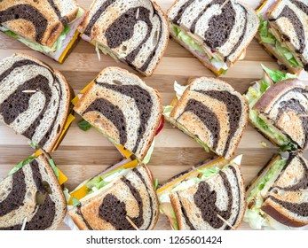 View from above of several simple appetizer sandwiches for a party using marbled rye bread with orange cheddar cheese, lettuce, apple slices, turkey meat and honey mustard on wood bamboo cutting board