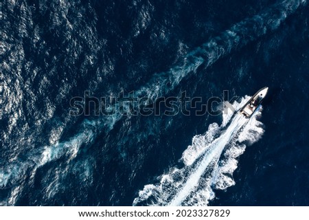 View from above, stunning aerial view of a boat cruising on a blue water creating a wake. Costa Smeralda, Sardinia, Italy.