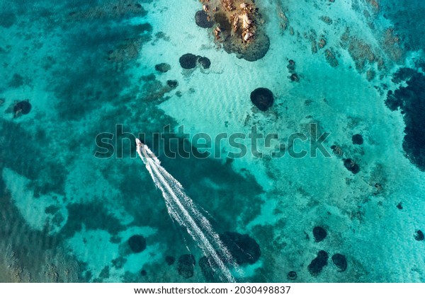 View from above, stunning\
aerial view of a boat sailing on a crystal clear, turquoise water.\
Giardinelli island, La Maddalena Archipelago, Sardinia,\
Italy.
