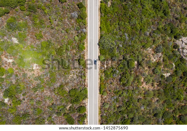 View from\
above, stunning aerial view of a car that runs along a road flanked\
by a green forest. Sardinia,\
Italy.