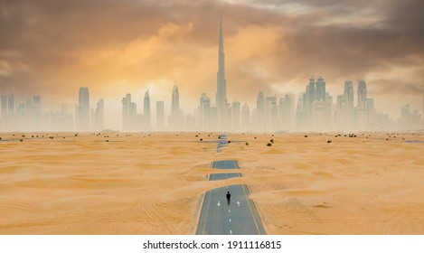 Näkymä ylhäältä, upea ilmakuva tuntemattomasta henkilöstä, joka kävelee autiolla tiellä, jota peittää hiekkadyynit, taustalla Dubai Skyline. Dubai, Yhdistyneet Arabiemiirikunnat.