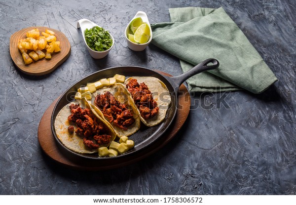 View from\
above of tacos al pastor served in hot iron skillet and accompanied\
by lemon, coriander and\
pineapple.