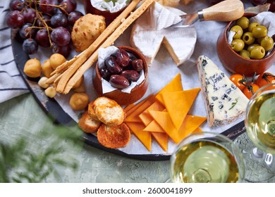 A view from above through the greenery of a large round Charcuterie Board and glasses of white wine on a green table