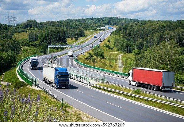 View from above of trucks\
driving on the highway with electronic toll gates in a wooded\
landscape.