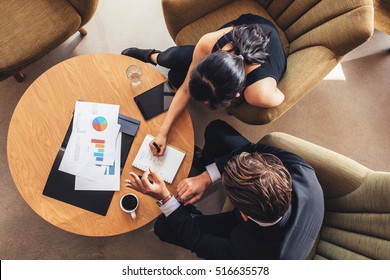 View From Above Of Two Business People Planning Work Around Table. Businessman And Woman Going Through The To Do List While Sitting At Office Lobby.