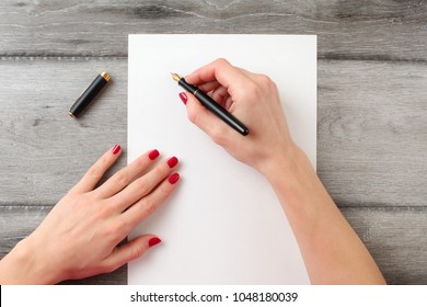 View from above to woman's hands with red nails, holding black fountain ink pen with gold nib, ready to write something on empty piece of paper laying on gray wood table. - Powered by Shutterstock