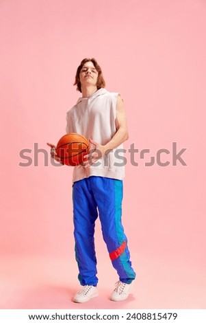View from above of young man, basketball player in retro uniform warming up before game against pastel pink studio background. Concept of active lifestyle, sport and recreation, hobby. Ad