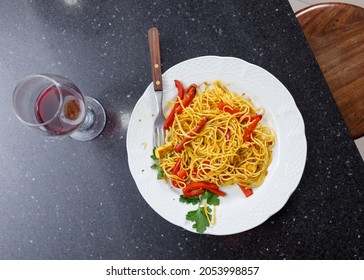 View From Above.Marble Table With Plate Of Rice Noodles With Curry, Red Bell Peppers And Parsley, And Glass Of Red Wine. Vegan Food. Enjoying Healthy Food. No People.