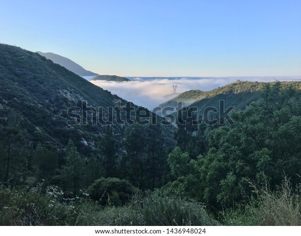 View across Angeles National Forest in southern\
California, high up with low clouds/fog in the valley below and a\
power pylon visible