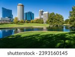 View across green planting of Gateway Arch park and across the lake to office buildings and hotels in downtown St Louis Missouri