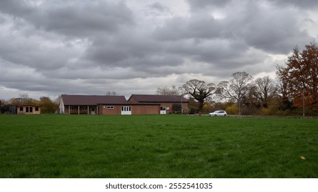 View across playing fields to a single story brick club house on a cloudy day with a treeline in background