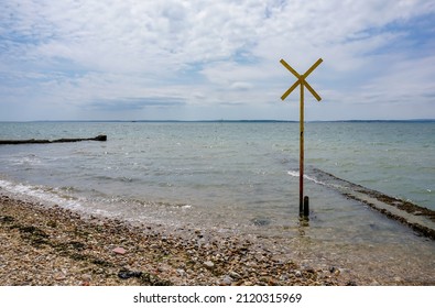 View Across River With A Warning Sign For Underwater Cables. Stony Shore Of Shipping River.