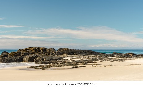 
View across sandy beach and rock to the sea beyond, with clouds on the horizon. Currumbin Beach, Queensland, Australia. 
