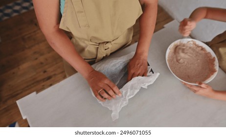 View of adult hands lining a baking sheet and a child mixing batter in a white bowl. A cooking scene in a warm and inviting kitchen environment. - Powered by Shutterstock