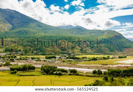 View from afar of the city of Paro, with buildings, houses, rice fields, by the river in Bhutan 