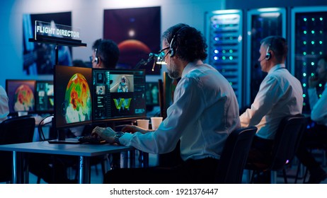 View Of Aged Man Giving Advice To Mature Coworker Using Computer During Spacecraft Launch In Flight Control Center