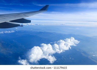 view from airliner window with white clouds and mountain range