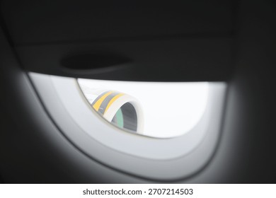View of airplane engine through partially closed window shade.