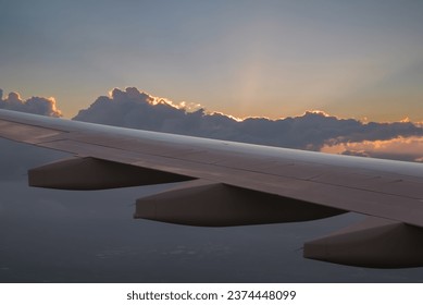 The view from the airplane window to the clouds and sunset. Clean photo no logos or brandnames. View of white wing of aircraft flying in blue sky betwen  colorful fluffy cumulus clouds in sunset