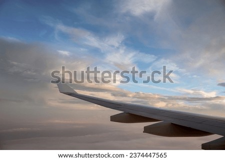 The view from the airplane window to the clouds and sunset. Clean photo no logos or brandnames. View of white wing of aircraft flying in blue sky betwen  colorful fluffy cumulus clouds in sunset