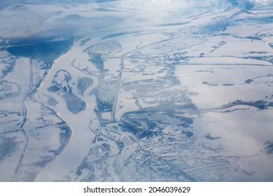 View From The Airplane Window At Dawn To Snow-covered Siberia. Blue Tint, River, Forest. The Texture Of The Winter Landscape From The Side Of The Plane.