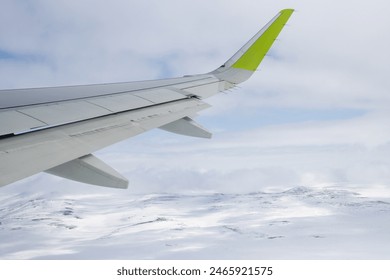 View of an airplane wing and snow-covered hills. Flight over snow-capped mountains. An airliner gaining altitude. Traveling by plane to the Arctic. Passenger air transport. - Powered by Shutterstock