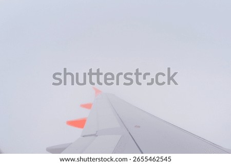 View from an airplane wing soaring through a thick cloud cover on a gray day over an undisclosed location in the sky