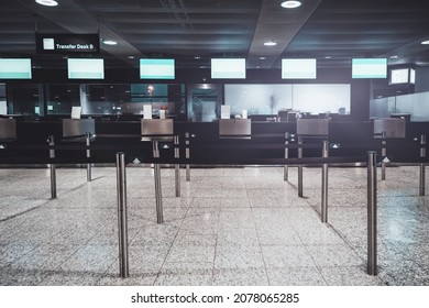 View Of An Airport Check-in Area With Multiple Empty Decks For Transfer Passenger Service And Empty Plasma TV Screens On The Top; Chromium Poles Of Portable Fencing In The Foreground, Neon Light