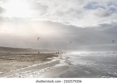 view along the beach next to the Kennemerland National Park, Haarlem, Netherlands. Kitesurfers and other peolple on the beach. Mist from the sea in the air, strong sunlight