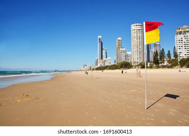 View Along The Beach Of Surfers Paradise On The Gold Coast With Few People On The Beach, High Rise Building To The Right And Beach Flag In Front