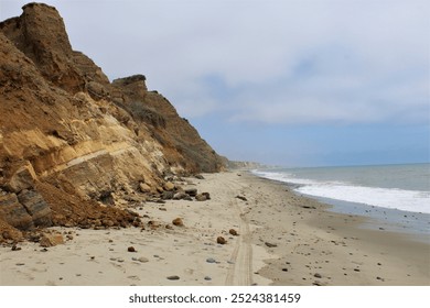 A view along the California coastline of red rocky cliffs, sandy beach, and breaking waves - Powered by Shutterstock