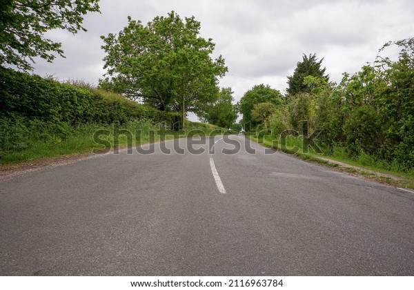 view\
along quiet country lane. Empty road with trees and hedges at the\
sides. Middle of a road. Road trip in rural\
England.