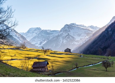 view of the alps from a valley in Glarus. Tödi peak with snow in the background, and grass fields with small barns in the front. Evening sunlight rays coming from the mountains. Bucolic warm winter - Shutterstock ID 1652522086