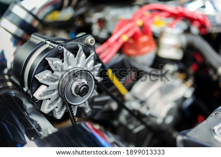View of an alternator in the engine of an old race car. Alternator is a type of electric generator used in cars to charge the battery and to power the electrical system when its engine is running.
